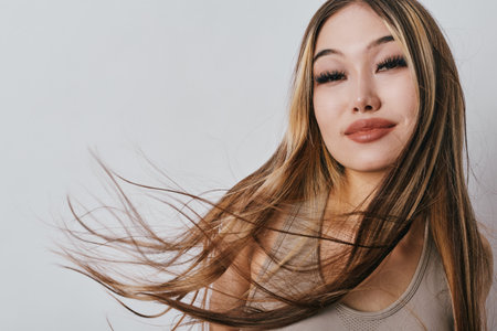 Woman with long hair and natural makeup posing with confident expression against white background. Closeup portrait of female model with smooth skin and loose brown hair.の写真素材