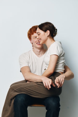 Couple sitting and hugging on chair with smiles and affection in studio setting. Young man and woman...