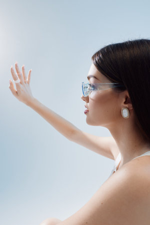 Profile of a young woman in clear glasses and elegant earrings reaching out with her hand against a...