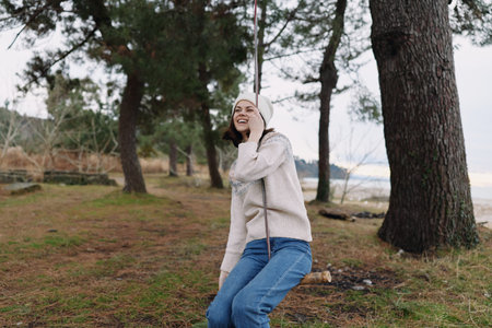 Woman outdoors in a forest by the coast, wearing a cozy sweater and jeans, smiling softly while enjoying nature and a relaxed pose.の写真素材