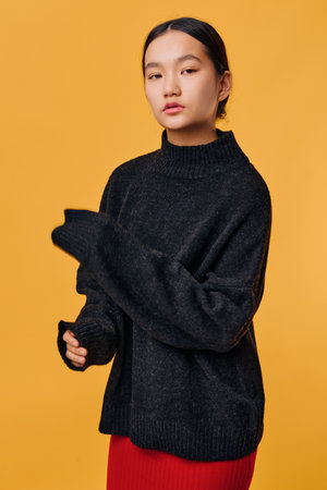 Young woman in black oversized sweater standing against orange background with serious expression,...
