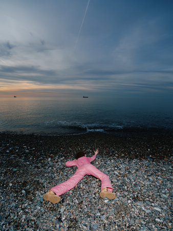 Beach scene with a pink plush toy lying on pebbles as waves meet the shore at dusk, calm sky and...