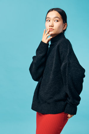 Young woman in black oversized sweater and red skirt posing against blue background looking sideways...