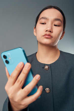 Young woman using smartphone with focus on screen in casual outfit. Female holding mobile phone for...