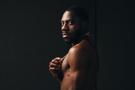 Creative visual designer style portrait of African American man with dark skin looking at camera with confident expression and muscular body on black background.の写真素材