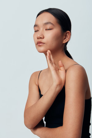 Woman with closed eyes and calm face in black sleeveless top posing with raised hand on light background. Beauty, serenity, relaxation, skin care, mindfulness and meditation concept portrait.の写真素材