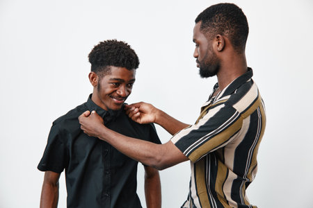 Two african men with dark skin adjusting shirt collar and smiling in studio. Friends, casual clothing and grooming with positive interaction and care between young males.の写真素材