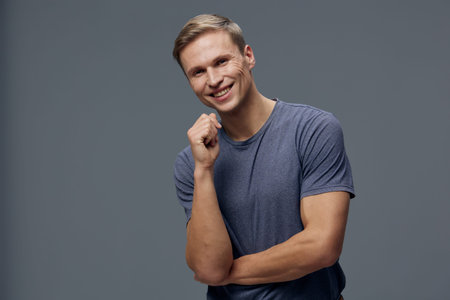 Smiling cheerful man with short hair wearing casual blue T-shirt posing against plain gray background, looking directly at camera, happy facial expression, studio portrait, relaxed mood, lifestyle concept.の写真素材