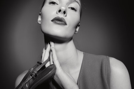 Portrait of a fair skinned Caucasian woman holding a high heel shoe near her neck in a black and white studio setting. Concept of fashion, elegance, and minimalism.の写真素材