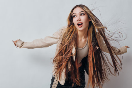 Young woman with long brown hair and dreadlocks wearing stylish beige jacket and light top posing with hair flying on white background in studio.の写真素材