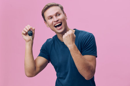 cheerful young caucasian man holding car key fist pump wearing blue t-shirt excited pink background digital nomad conceptの写真素材