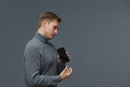 serious young caucasian man wear gray knit turtleneck hold black smartphone gesture finger isolated on gray background studio portrait digital detox conceptの写真素材