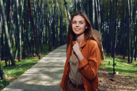 Woman with backpack smiling on a forest path, portrait of a young hiker outdoors surrounded by trees and sunlight.の写真素材