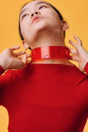 Woman with red ribbon around neck in red top on yellow background, hands touching neck, closeup portrait with minimal style and bright color contrast in studio light.の写真素材
