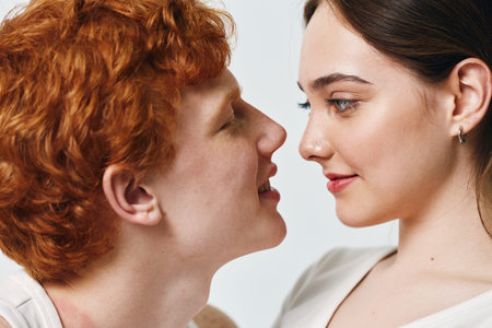 Young couple closeup with red hair man and brunette woman looking at each other, intimacy and connection in studio with light background for love and relationship.の写真素材