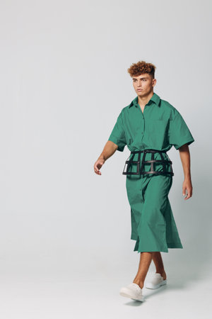 Young man walking in green oversized shirt and matching wide pants with white sneakers on plain background. Fashion model with curly hair showcasing modern casual outfit in studio.の写真素材