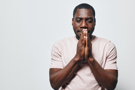 African American man with dark skin and beard standing with hands pressed together in prayer...