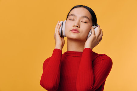 Young woman wearing headphones and closed eyes enjoying music with calm face, standing against...