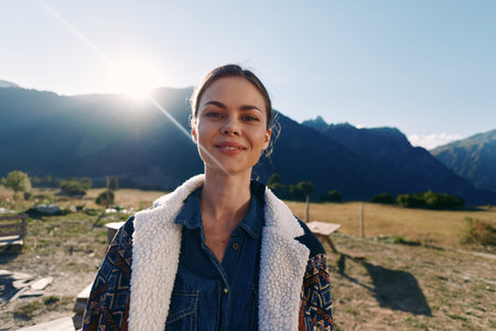 Woman portrait with smile in mountains at sunrise outdoors, nature traveler wearing denim and shearling jacket, happy young adult enjoying rural landscape and fresh morning lightの写真素材