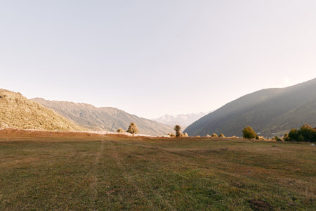Meadow valley mountains grass landscape hills sky sunrise captured in warm morning light over a wide...