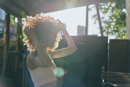 silhouette of woman with curly hair adjusting her hairstyle outdoors in sunlight, casual outfit,...