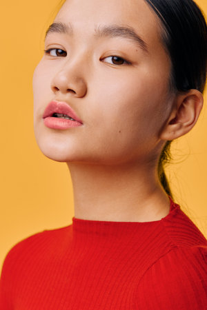 Portrait of young woman in red sweater with smooth skin and natural makeup, closeup on face and confident expression against orange background in studio with soft lighting.の写真素材