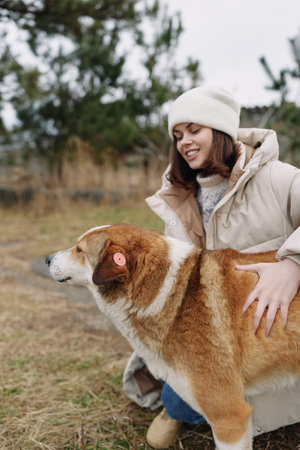 Woman in a warm coat and beanie enjoying a winter outdoors moment with a large dog in a grassy...