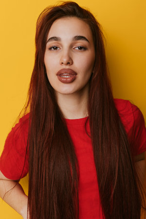 Young woman with long straight hair and full lips wearing red shirt posing against yellow background...