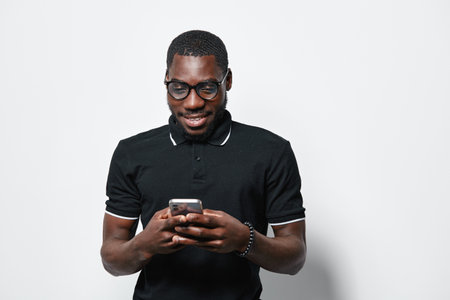 African American man with dark skin and glasses wearing black polo shirt using smartphone and...