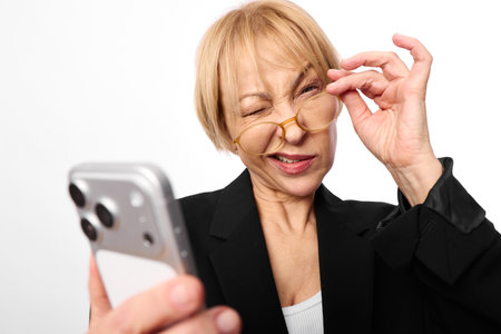 Confident middle aged woman with short blonde hair wearing glasses and black blazer holds smartphone...