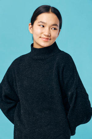 Young woman wearing black sweater posing with hands behind back looking sideways smiling on blue...