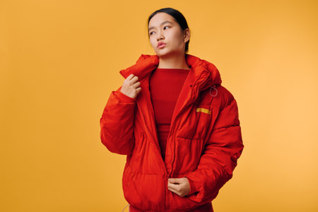 Woman wearing red puffer jacket looking to side on yellow background. Casual clothing style with...