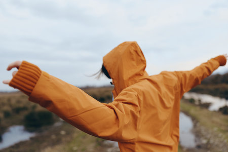 Woman lifestyle concept with a person in orange raincoat spreading arms outdoors on a cloudy day....