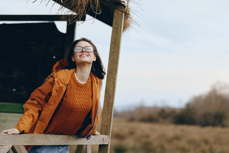 Young woman lifestyle enjoying fresh air outdoors, wearing glasses and orange jacket, smiling with...