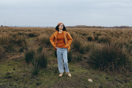 Young woman lifestyle standing in open field wearing orange jacket and headband. Casual fashion...