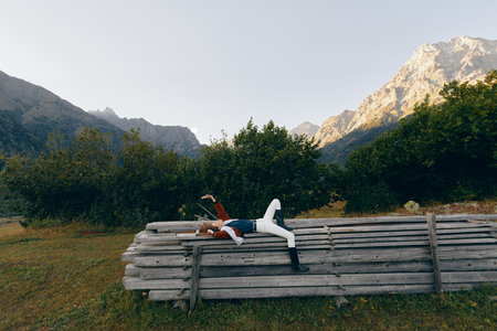 Person lying on wooden bench in mountains nature meadow, relaxing outdoors among trees and alpine...
