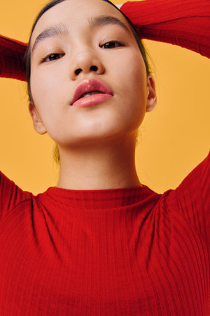 Woman portrait looking down with confident expression wearing red sweater on yellow background....