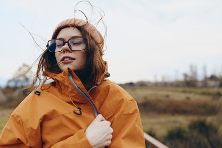 Young woman lifestyle portrait outdoors wearing orange jacket and glasses, enjoying fresh air with...