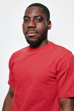 Portrait of confident black man with dark skin wearing red t shirt looking at camera isolated on...