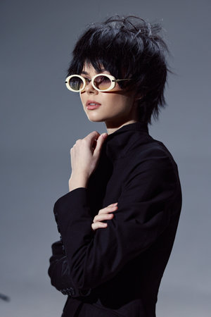 Stylish woman with short black hair wearing sunglasses and a black turtleneck expresses confident...