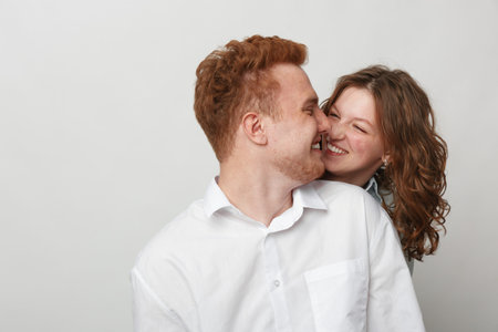 Happy young couple with red hair and curly hair smiling and embracing each other on white...