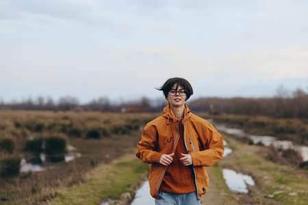 Young woman lifestyle outdoors in autumn wears orange jacket and sweater walking on rural path....