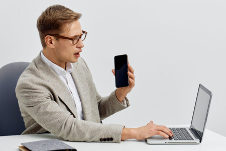 Man using laptop and holding smartphone in modern office, professional workspace, technology,...
