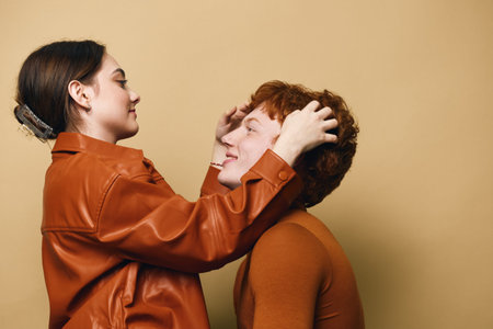 Woman and man in casual clothes smiling and touching each others heads against beige background....