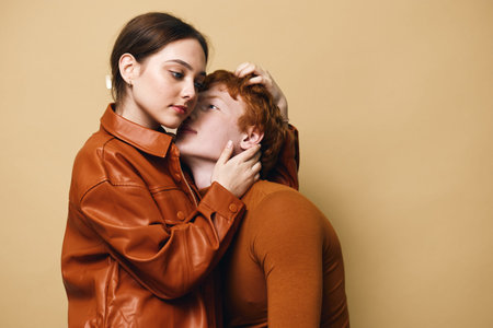 Couple in brown and orange clothing, woman gently holding manâ€™s head with affection, studio...