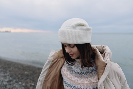 Woman in a knit sweater and warm coat on a windy beach, winter landscape by the sea, soft light and...