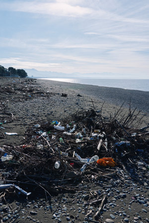 Beach scene with litter and debris along a pebbled shore, polluted coastline by the ocean, driftwood...
