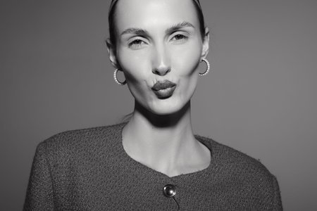 White woman with pale skin and slicked back hair makes a kissy face in studio black and white...