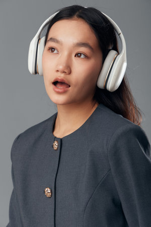 Young woman with headphones listening to music and enjoying sound with open mouth in casual outfit on neutral background. Female portrait with audio technology and entertainment concept.の写真素材