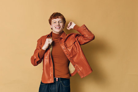 Young man with short red hair wearing orange leather jacket and turtleneck smiling with raised fist...